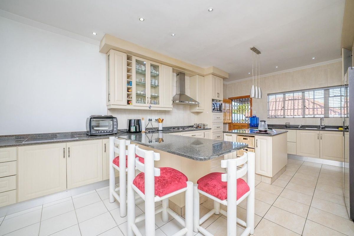 Spacious kitchen featuring cream cabinetry, granite countertops, a central island with breakfast bar, and integrated appliances, finished with neutral floor tiles.