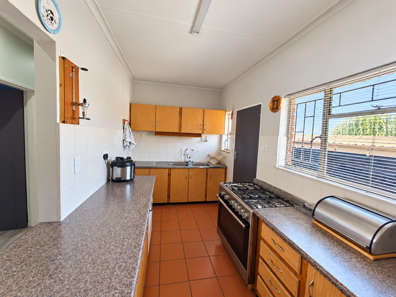 A functional kitchen featuring wooden cabinetry, laminate countertops, a gas stove, and tiled flooring with a large window providing natural light.