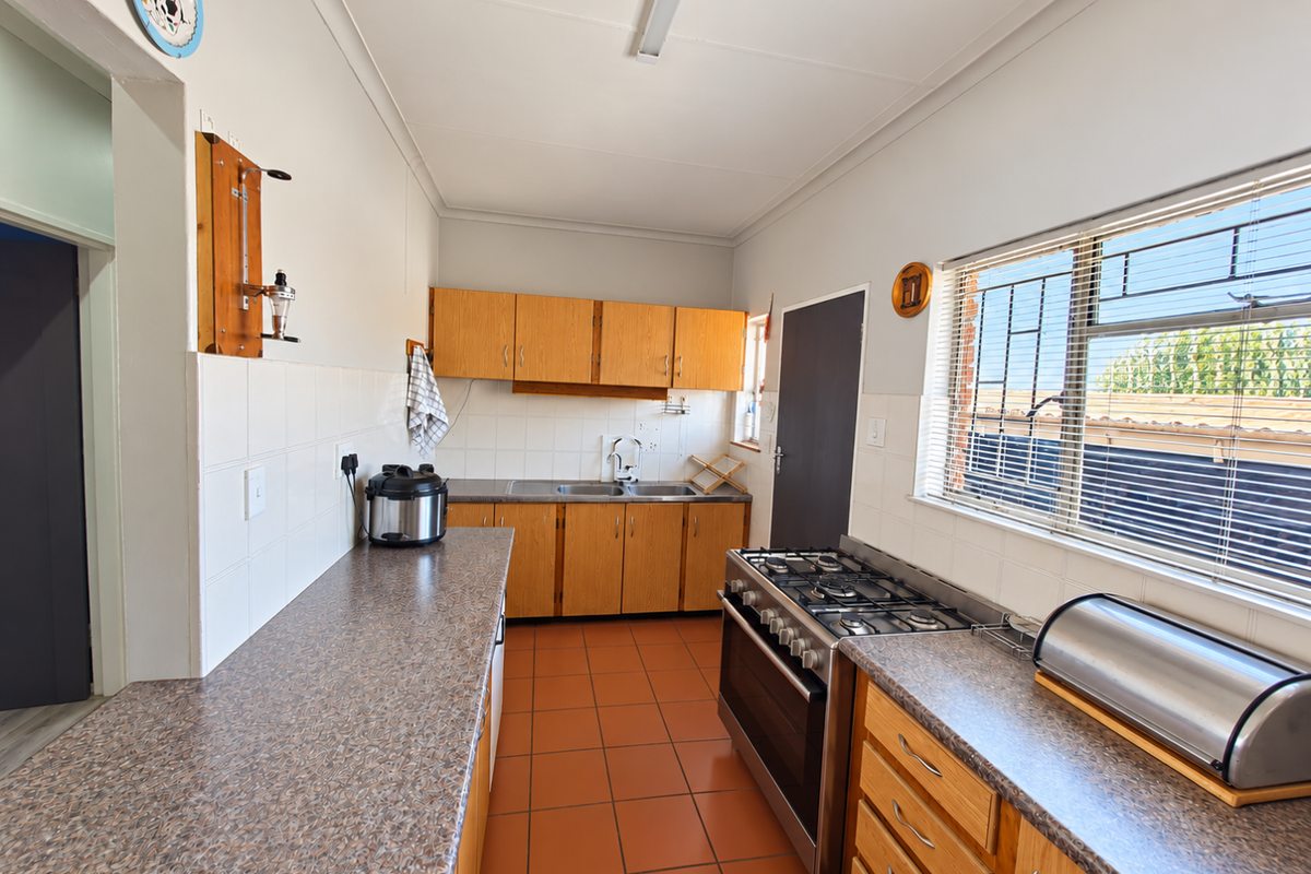 A functional kitchen featuring wooden cabinetry, laminate countertops, a gas stove, and tiled flooring with a large window providing natural light.