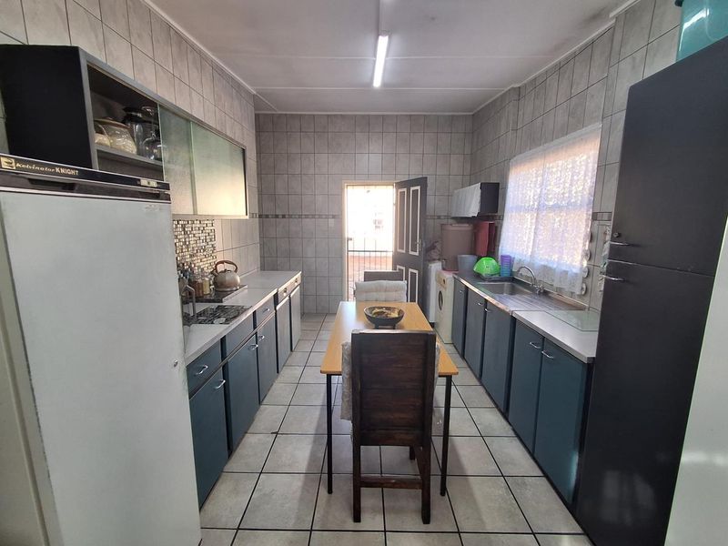 Functional kitchen featuring tiled walls and floors, ample built-in cabinetry, and a stainless steel sink, with direct access to the exterior.