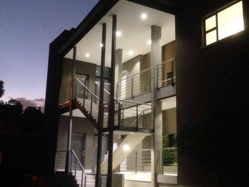 Modern multi-level apartment building exterior at dusk, featuring a prominent external staircase with stainless steel balustrades and integrated recessed lighting.