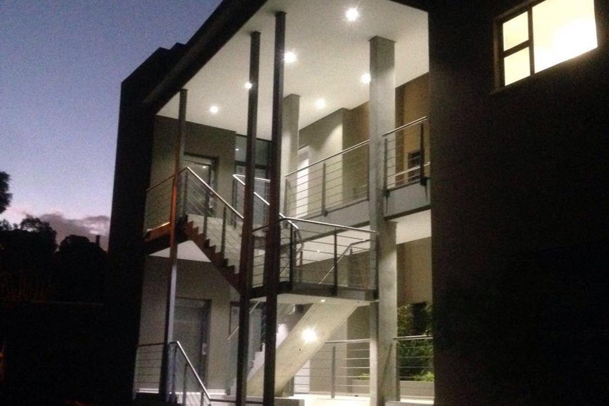 Modern multi-level apartment building exterior at dusk, featuring a prominent external staircase with stainless steel balustrades and integrated recessed lighting.