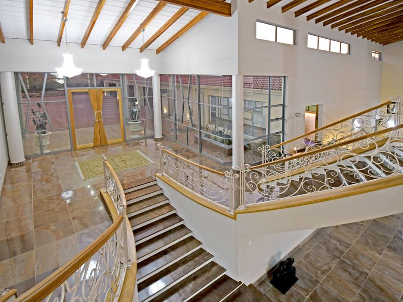 Spacious grand entrance hall featuring a sweeping staircase with ornate wrought iron balustrades, high ceilings with exposed timber beams, and extensive glass paneling.