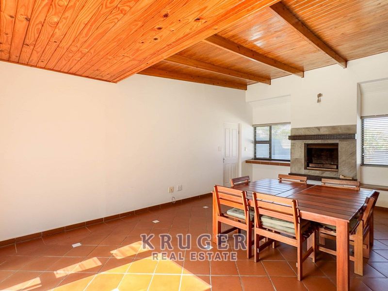 Spacious living area featuring a high exposed timber beam ceiling, stone fireplace, and tiled flooring with direct access to the exterior.