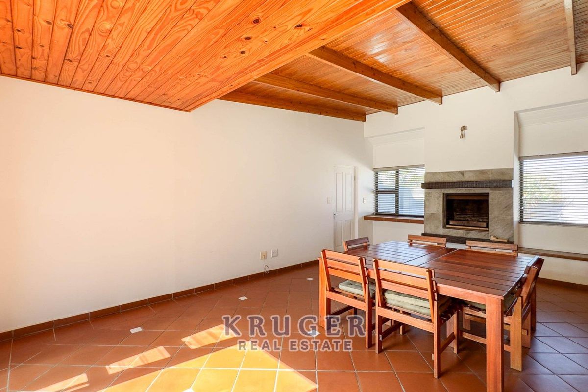 Spacious living area featuring a high exposed timber beam ceiling, stone fireplace, and tiled flooring with direct access to the exterior.