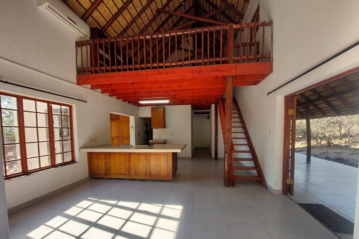Spacious open-plan living area featuring a high thatched ceiling, mezzanine level with timber staircase, and a functional kitchen island with built-in cabinetry.