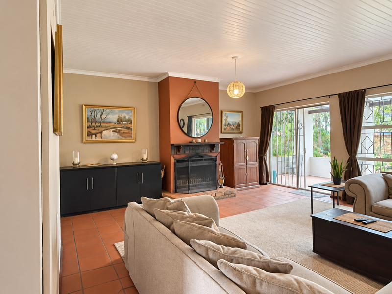 Spacious living room featuring a central fireplace with brick hearth, terracotta flooring, and large sliding glass doors providing access to the outdoor patio area.