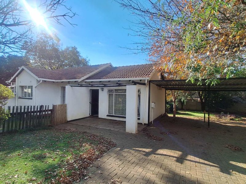 Front view of a single-story house featuring a tiled roof, paved driveway, attached carport, and a small covered patio area.