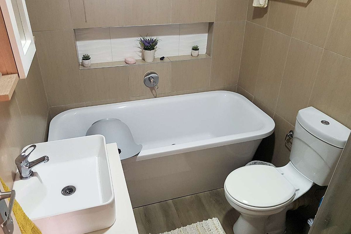 A compact bathroom featuring a modern vessel sink, a built-in bathtub with a recessed wall niche, and a standard toilet.