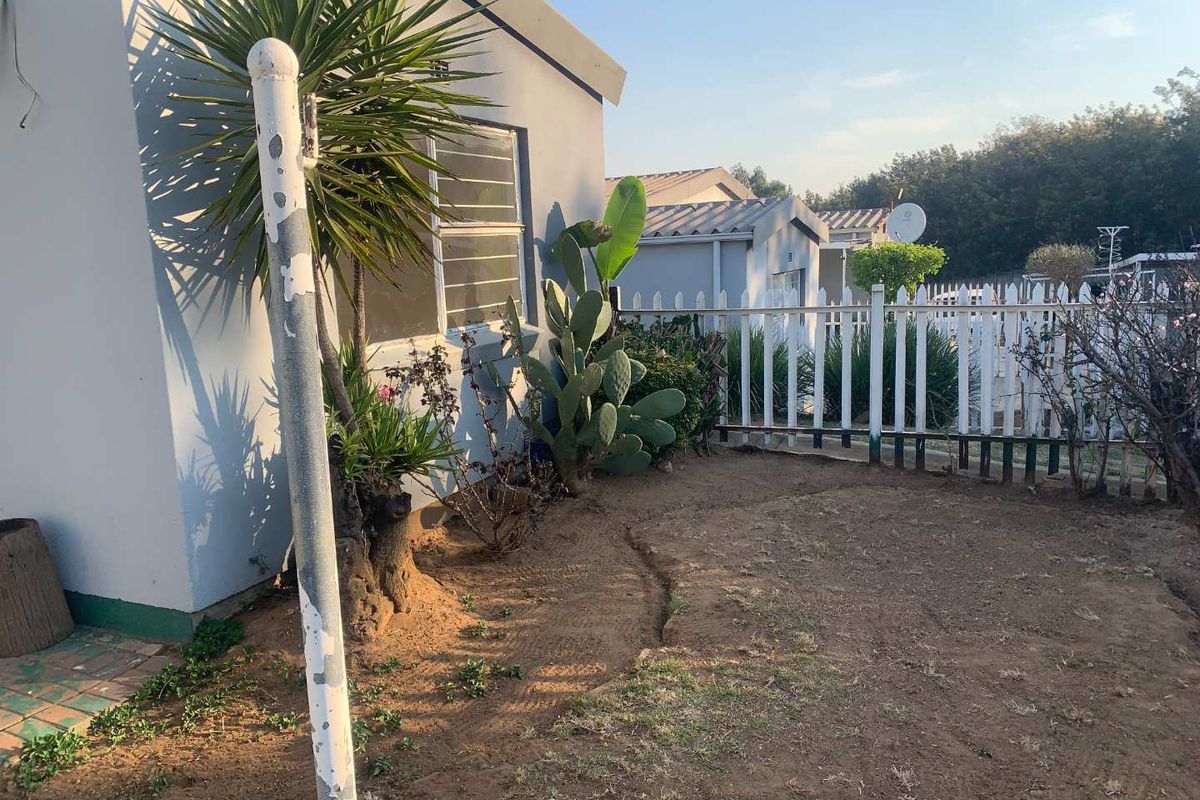 A view of the rear exterior area of the apartment, featuring a small garden space, white picket fencing, and a metal support pole.