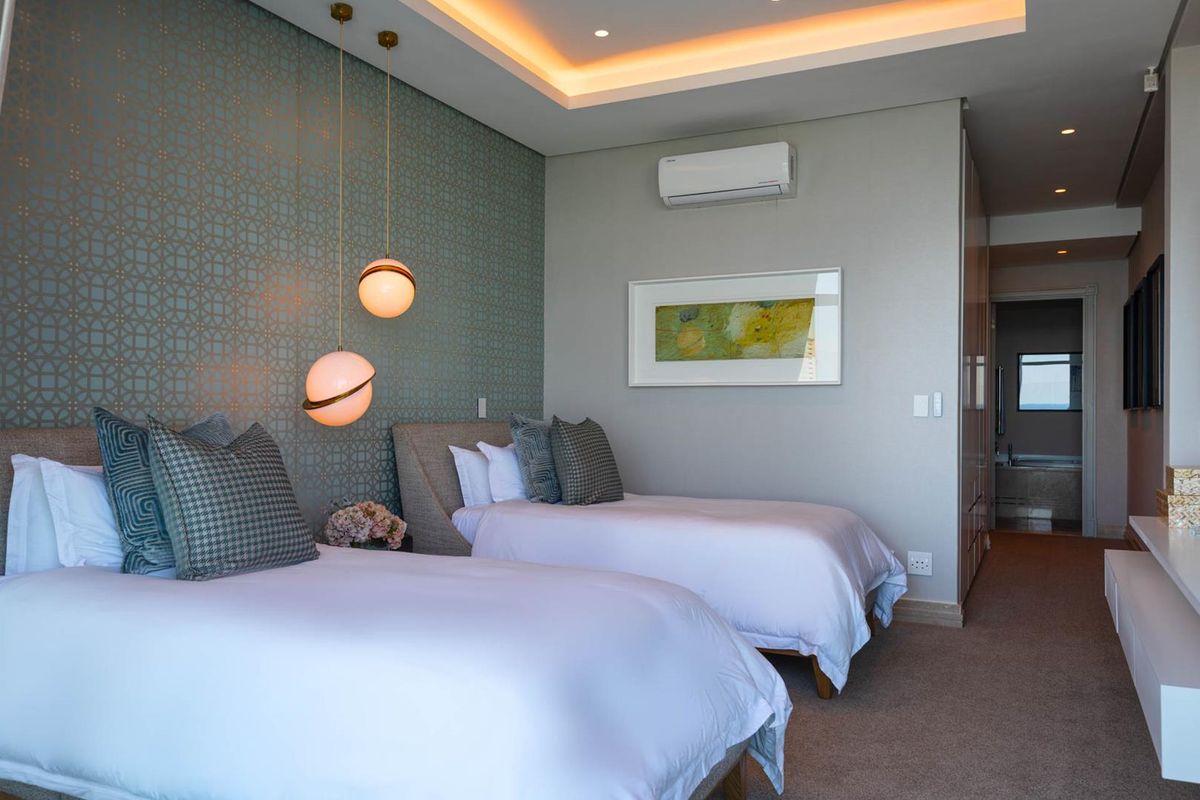 A well-appointed bedroom featuring recessed tray ceiling lighting, patterned accent wallpaper, and a wall-mounted air conditioning unit.