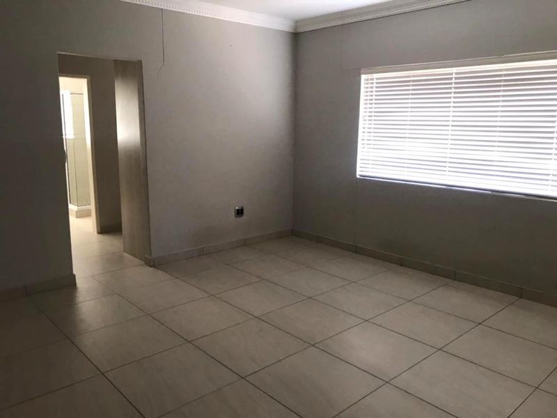 An empty bedroom featuring tiled flooring, venetian blinds, and decorative cornicing, with visible wall cracks requiring attention.