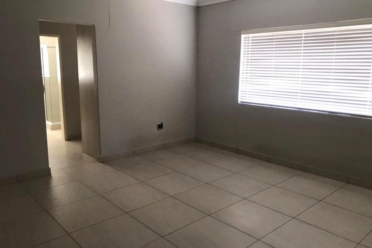 An empty bedroom featuring tiled flooring, venetian blinds, and decorative cornicing, with visible wall cracks requiring attention.