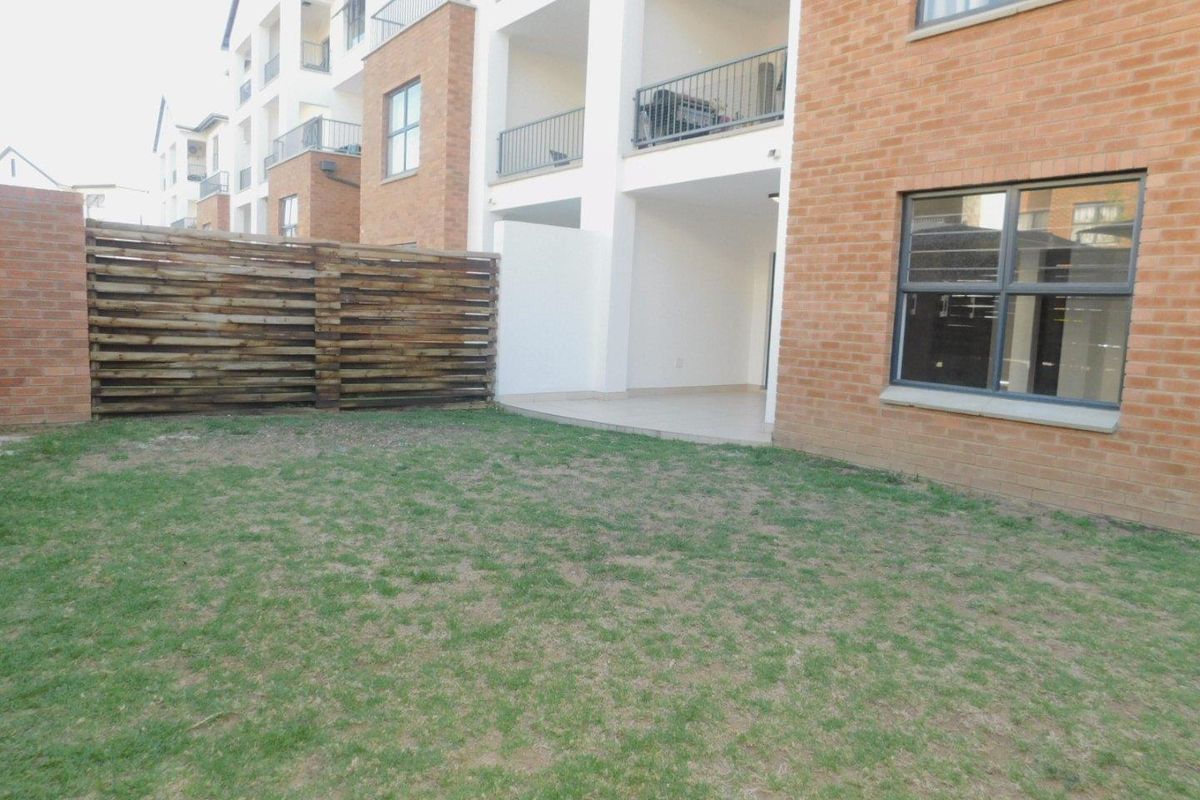 A rear view of the apartment building featuring a private garden area, a covered patio with tiled flooring, and a timber privacy screen.
