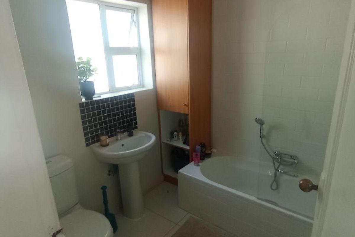 A functional bathroom featuring a pedestal basin, toilet, bathtub with a glass screen, and built-in storage cabinetry.