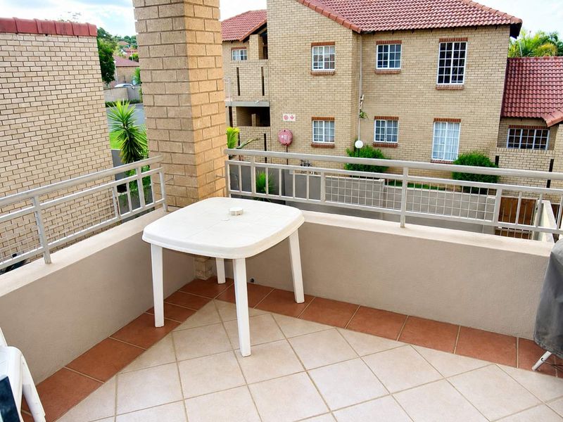 A private balcony featuring tiled flooring, a sturdy brick pillar, and a metal balustrade, overlooking the surrounding townhouse complex.