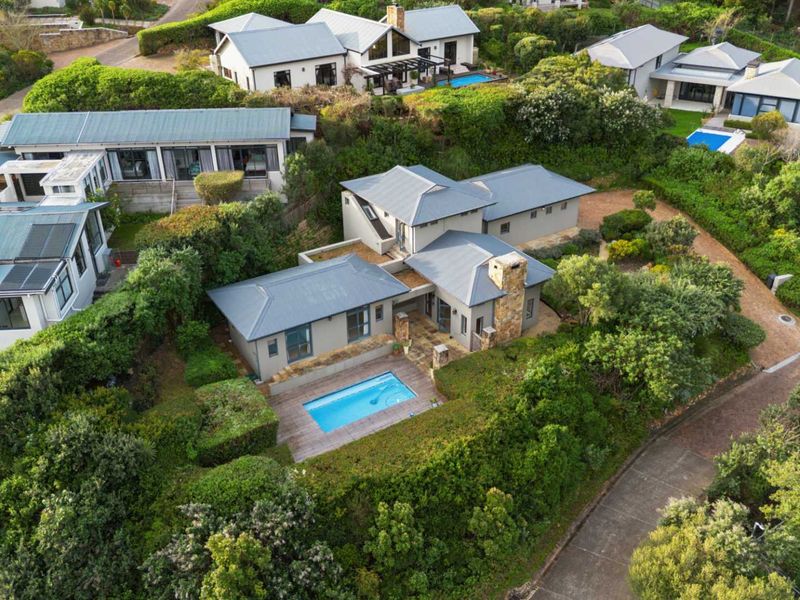 Aerial view of a residential property featuring a swimming pool, timber decking, and a stone chimney, set within a landscaped garden environment.