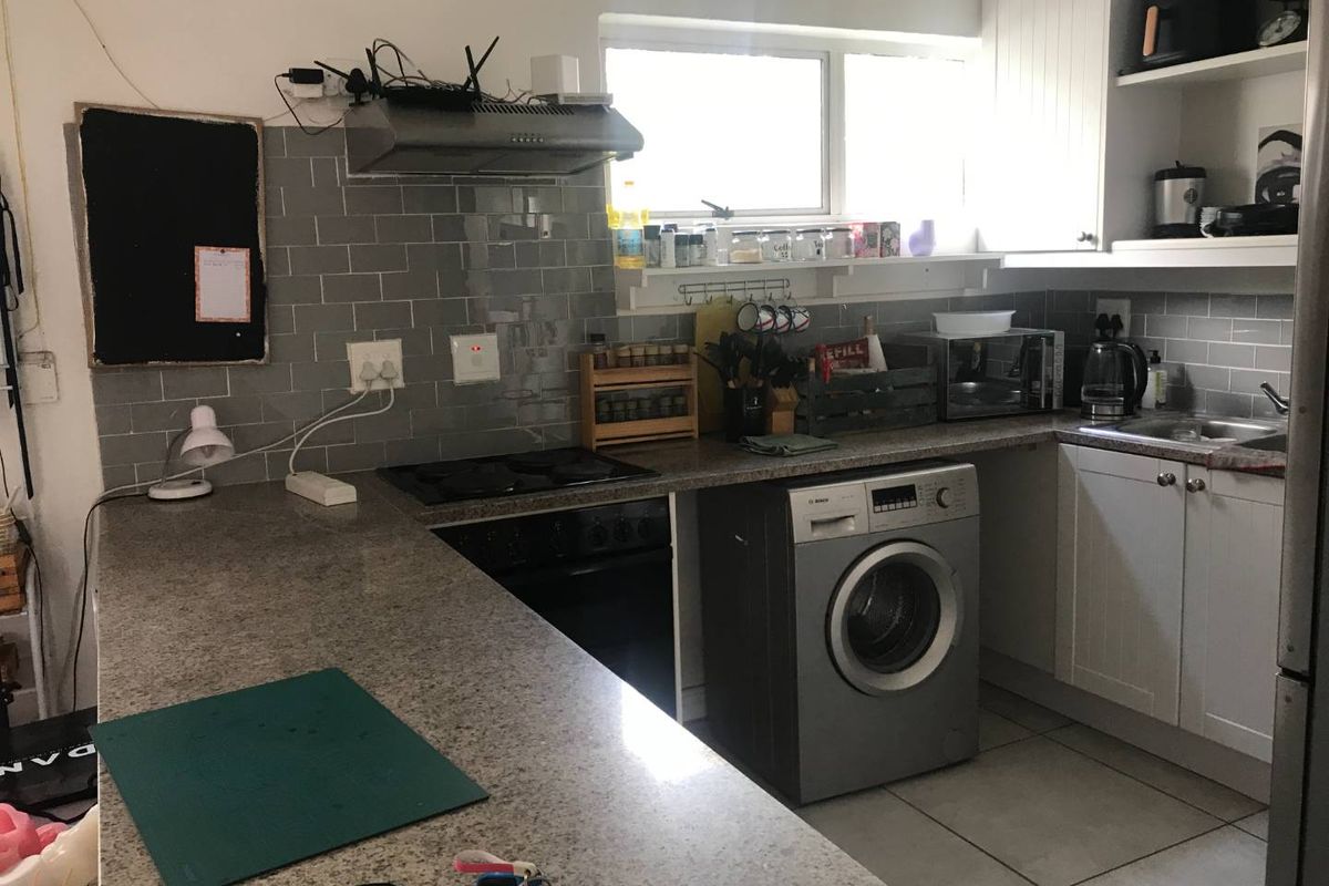 A functional kitchen featuring granite countertops, grey subway tile backsplash, built-in oven with extractor fan, and integrated laundry appliance space.