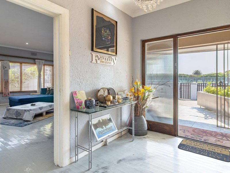 Entrance foyer featuring a sliding glass door with security gate, textured walls, and a decorative crystal chandelier, leading into the main living area.