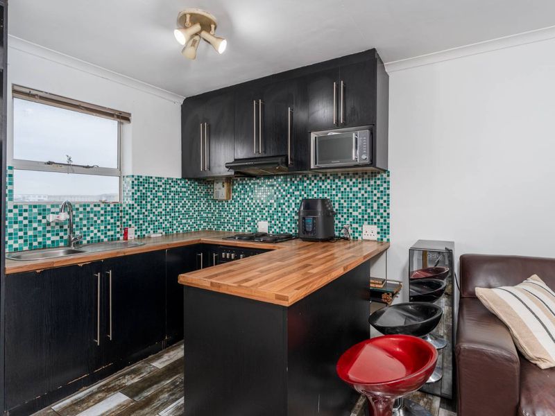 Compact kitchen featuring black cabinetry, wooden countertops, and a vibrant mosaic tile backsplash, offering a functional layout with integrated appliances.