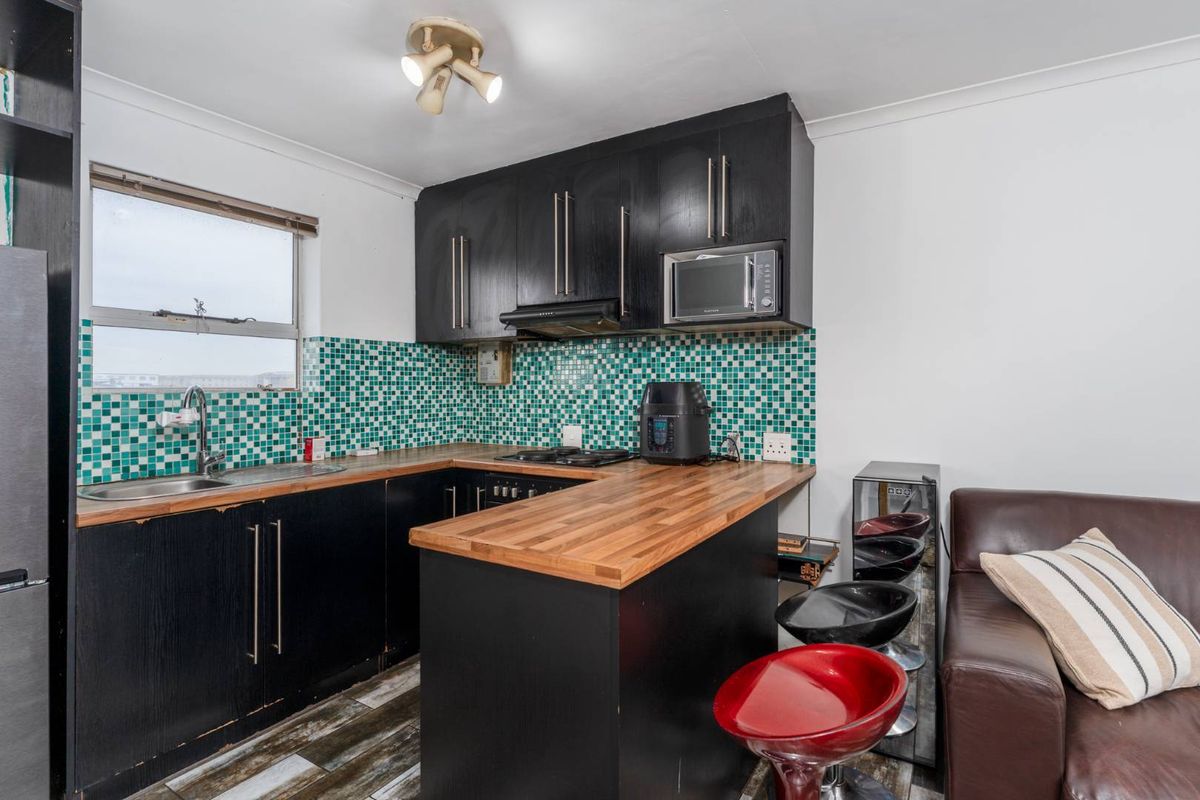 Compact kitchen featuring black cabinetry, wooden countertops, and a vibrant mosaic tile backsplash, offering a functional layout with integrated appliances.