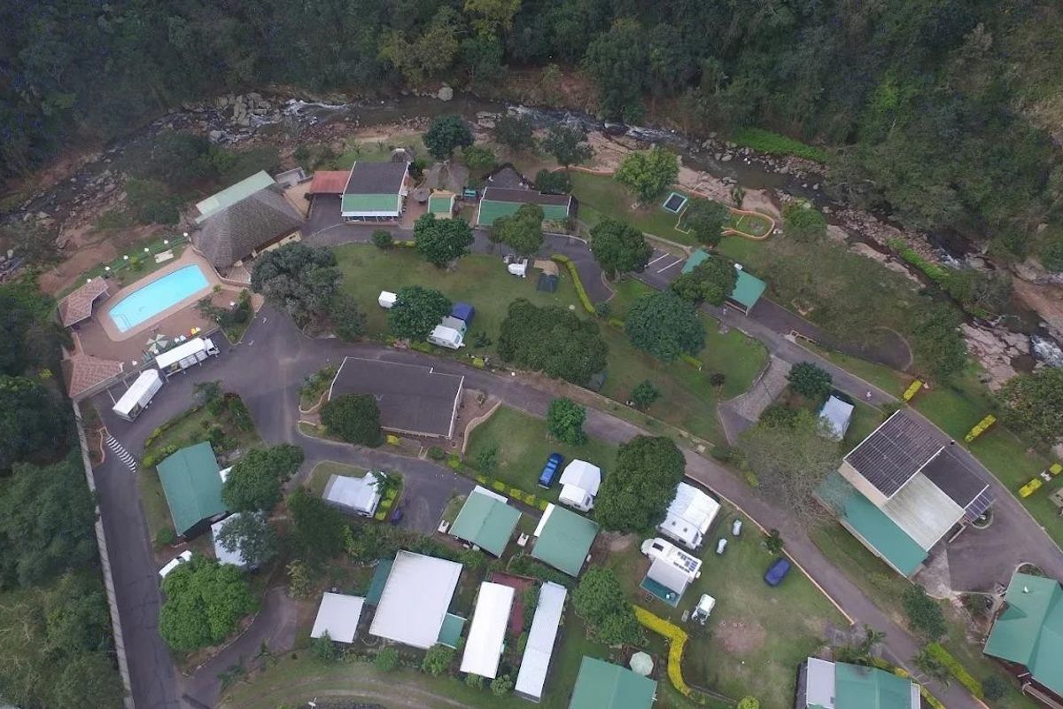 Aerial view of a sprawling property complex featuring multiple buildings, a swimming pool, landscaped grounds, and river frontage in a natural setting.