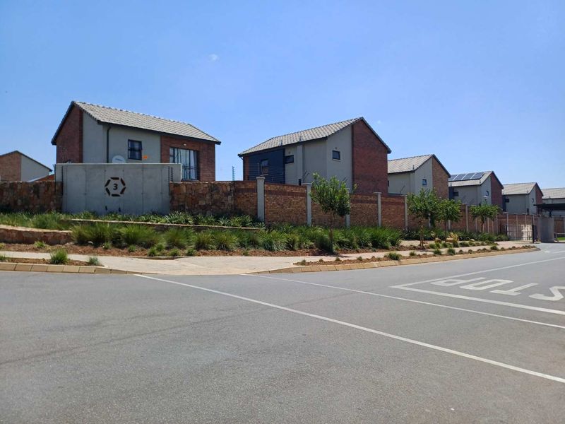 Street view of a residential estate featuring modern houses with brick and concrete boundary walls, tiled roofs, and established landscaping.