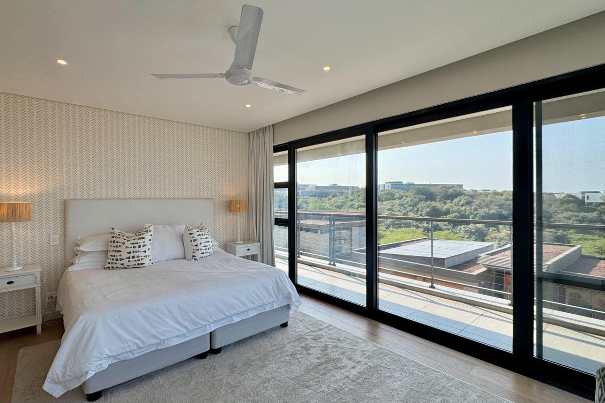 Spacious bedroom featuring modern wallpaper, recessed lighting, a ceiling fan, and large sliding glass doors opening onto a private balcony with scenic views.