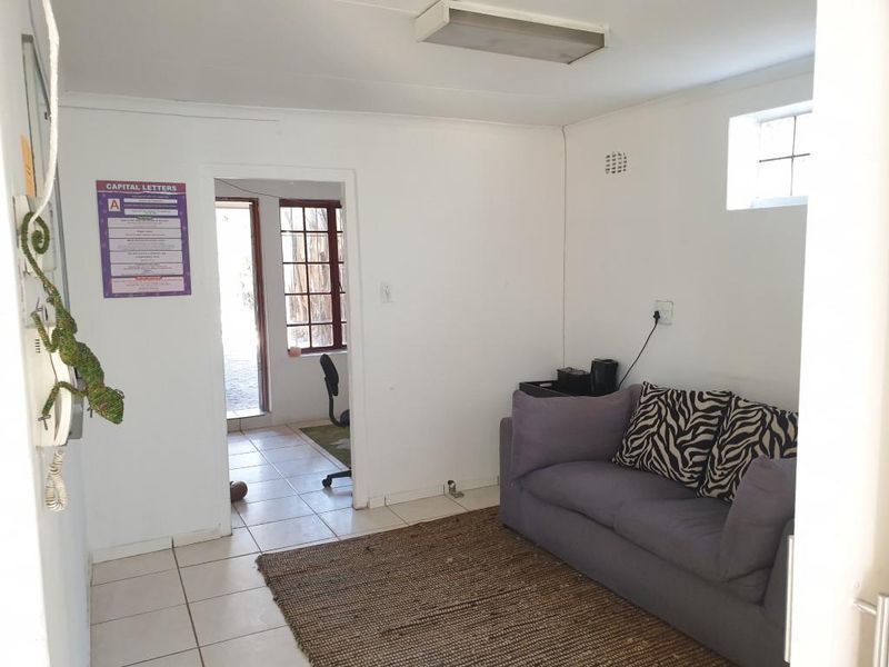 A functional office space featuring tiled flooring, a small high-level window, and direct access to an adjoining room.