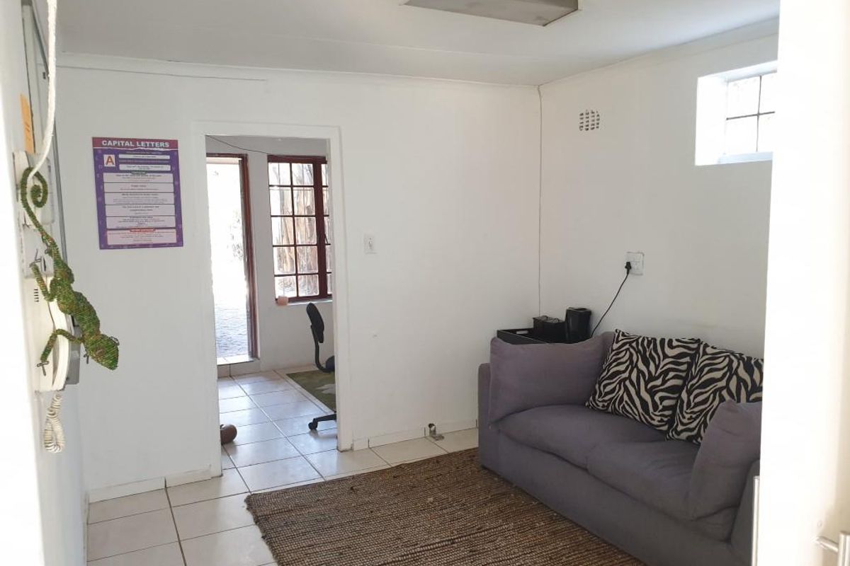 A functional office space featuring tiled flooring, a small high-level window, and direct access to an adjoining room.