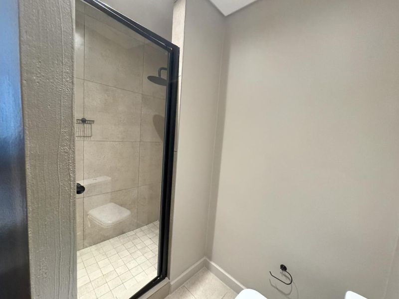 A modern bathroom featuring a walk-in shower with a black-framed glass screen, rain shower head, and neutral wall-mounted toilet.
