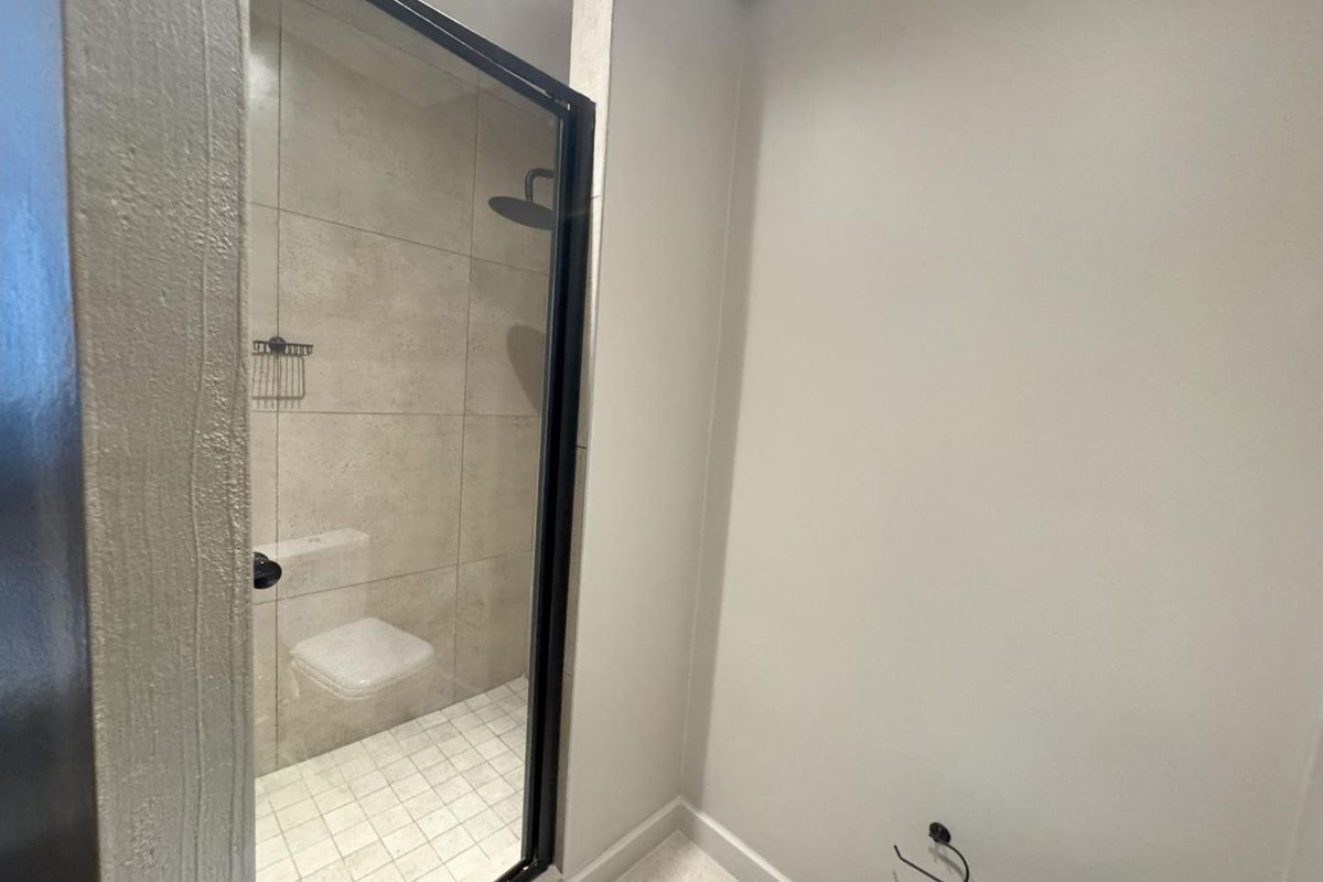 A modern bathroom featuring a walk-in shower with a black-framed glass screen, rain shower head, and neutral wall-mounted toilet.