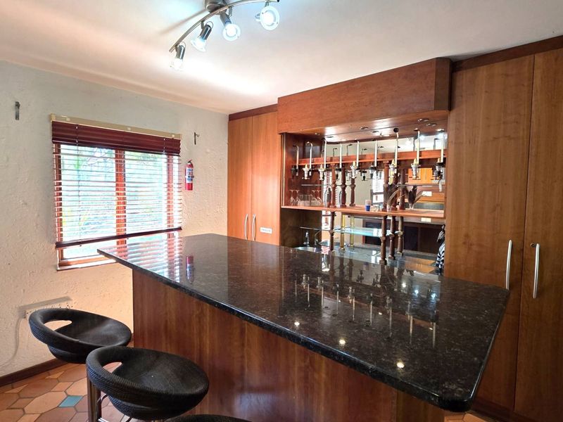 A dedicated home bar area featuring a granite-topped counter, extensive built-in cabinetry, mirrored shelving, and integrated bottle dispensers.