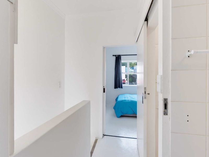 A bright hallway featuring a sliding door, white tiled wall section, and a towel rail, leading into an adjacent bedroom.