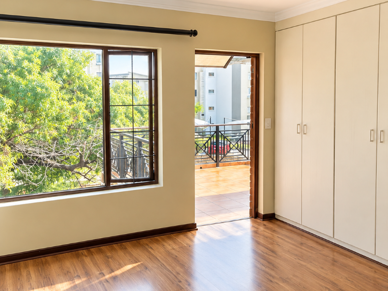 Bright and spacious bedroom featuring laminate flooring, built-in cupboards, and direct access to a private balcony.