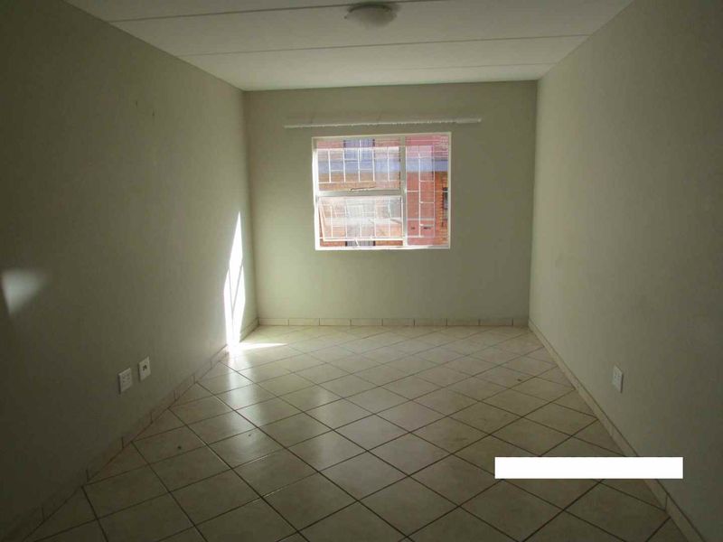 An empty bedroom featuring tiled flooring, neutral walls, and a window providing natural light.