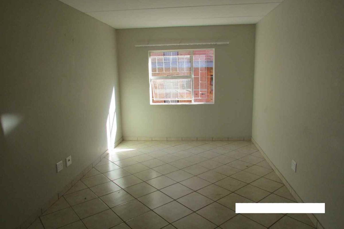 An empty bedroom featuring tiled flooring, neutral walls, and a window providing natural light.