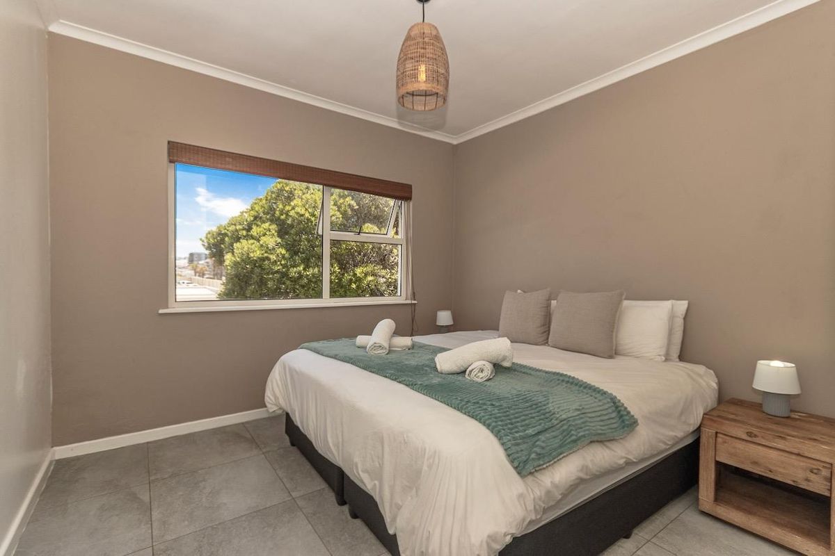 A well-maintained bedroom featuring neutral wall tones, tiled flooring, and a large window providing natural light and exterior views.