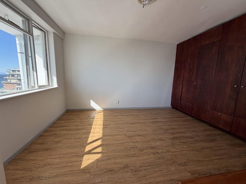A bright, empty bedroom featuring modern laminate flooring and dark wood built-in cupboards, offering a clean and neutral space ready for personalization.