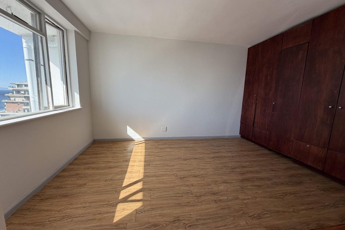 A bright, empty bedroom featuring modern laminate flooring and dark wood built-in cupboards, offering a clean and neutral space ready for personalization.