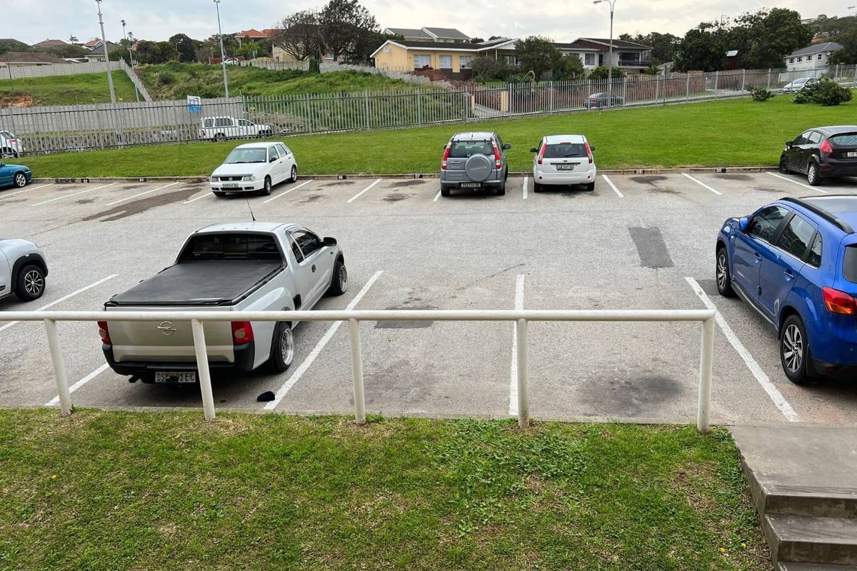 An outdoor parking area featuring asphalt surfacing, marked bays, and a metal safety railing, overlooking a grassed perimeter area.