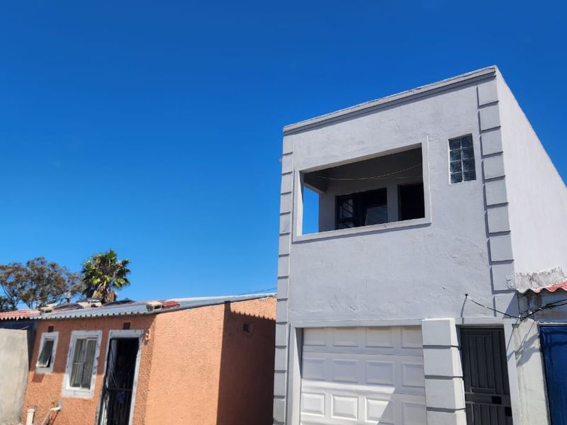 Front view of a two-story residential property featuring a garage, balcony, and adjacent single-story structure under a clear blue sky.