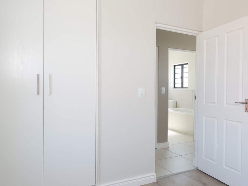 A clean, neutral bedroom featuring built-in wardrobes and direct access to an adjoining bathroom with tiled flooring.