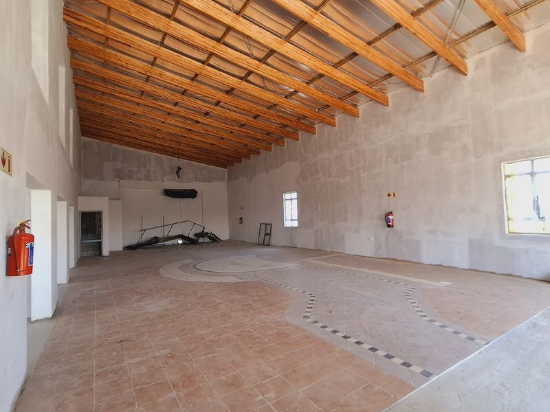 Spacious open-plan commercial area featuring exposed timber roof trusses, tiled flooring, and unfinished wall surfaces, suitable for various business applications.