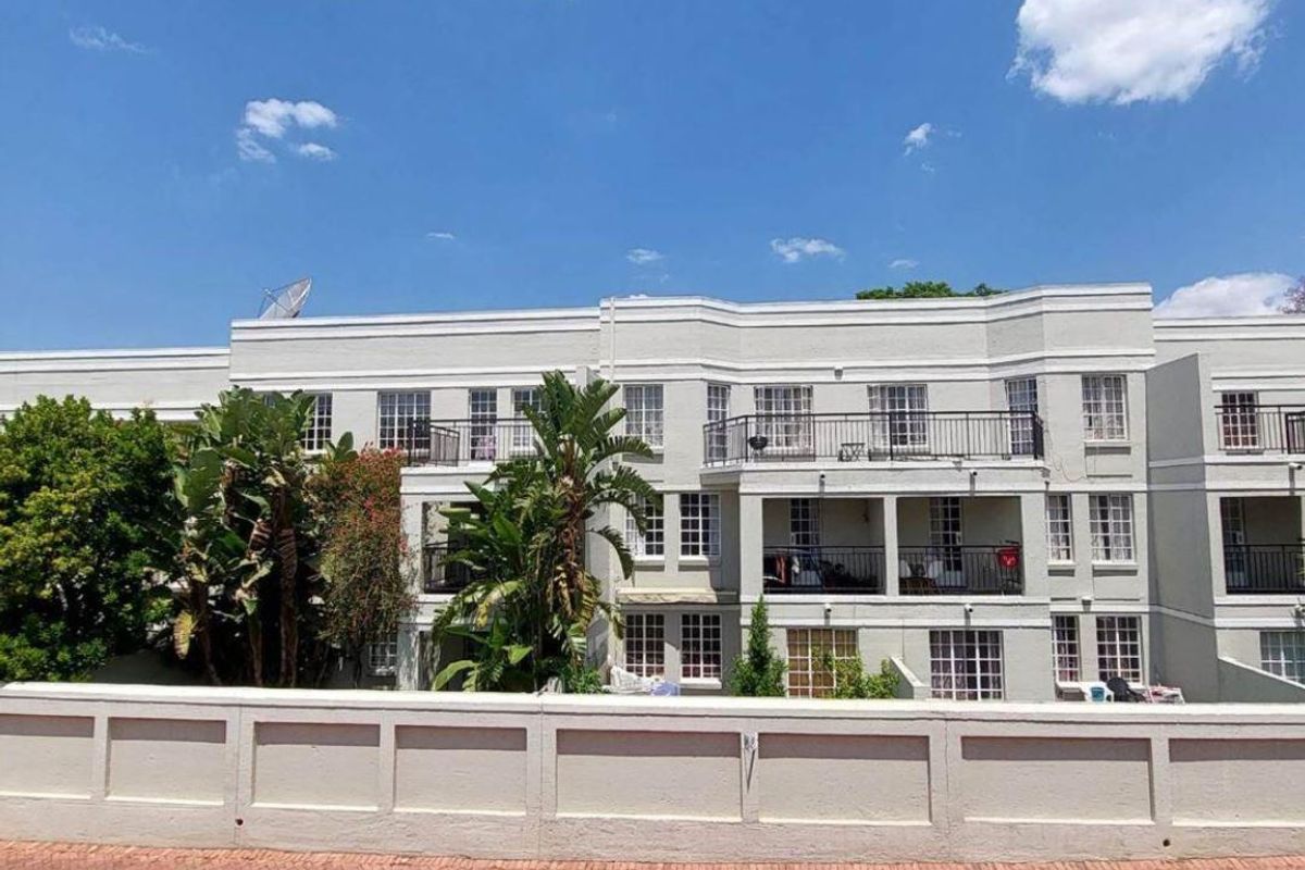 Rear elevation of a multi-story apartment complex featuring private balconies, metal railings, and multi-pane windows overlooking a landscaped area.