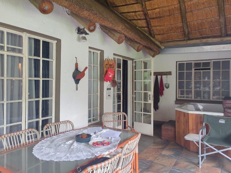 Covered patio area featuring a thatched roof, exposed timber beams, tiled flooring, multiple french door access points, and a built-in jacuzzi.