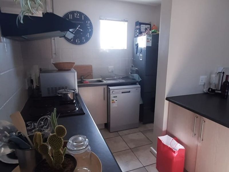 A functional kitchen featuring light-toned cabinetry, dark laminate countertops, ceramic tile flooring, and essential built-in appliances including a hob and extractor fan.