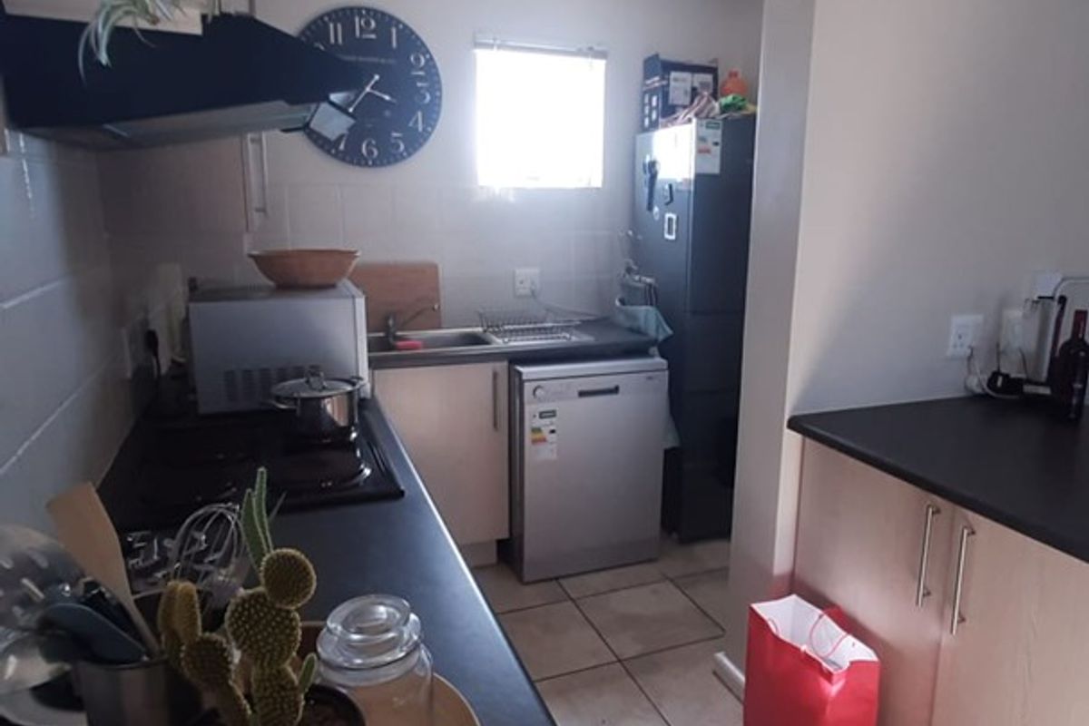 A functional kitchen featuring light-toned cabinetry, dark laminate countertops, ceramic tile flooring, and essential built-in appliances including a hob and extractor fan.