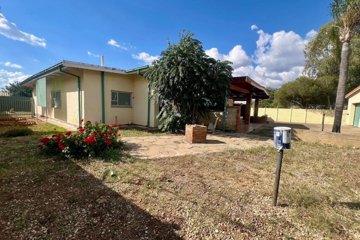Rear view of the property featuring a paved courtyard, covered patio area, and a built-in brick braai, set within a spacious garden.