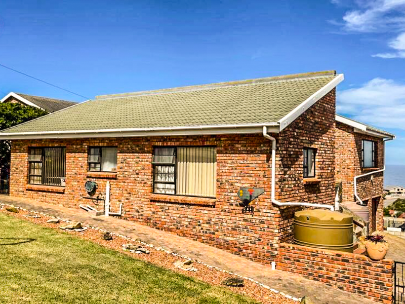Rear view of a face brick house featuring a tiled roof, rainwater tank, and paved walkway with coastal views in the background.
